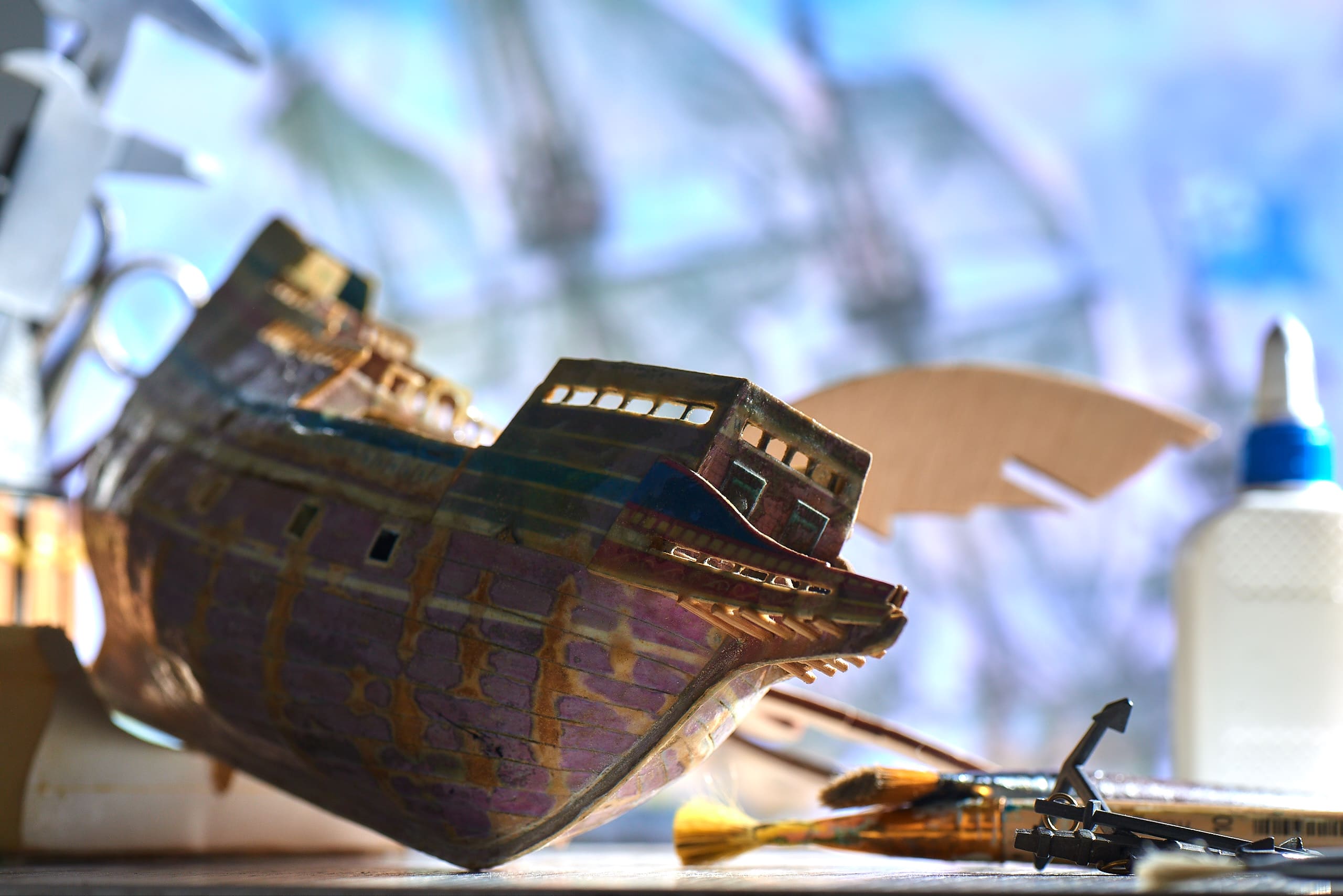 Wooden ship model under construction with modeling tools and paints.