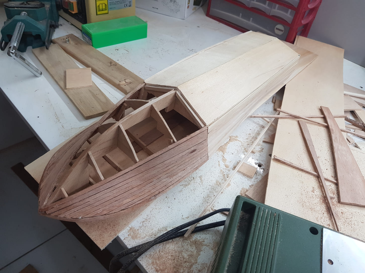 Scafo in legno in fase di applicazione del secondo fasciame, con listelli curvati e strumenti da modellismo